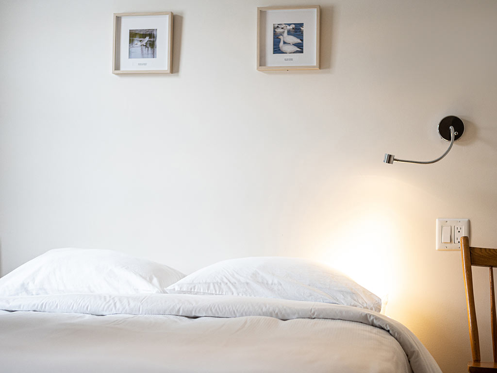 Gros plan sur un lit avec literie blanche et tête de lit en bois à l'Espace du Carmel