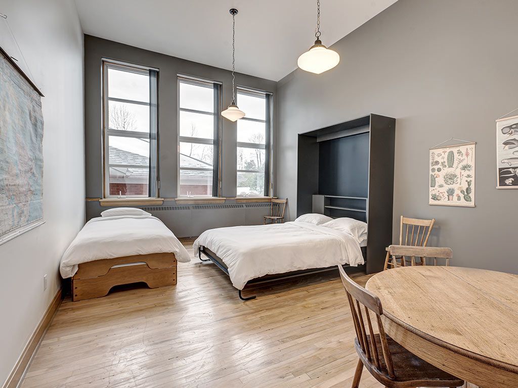 Chambre lumineuse avec deux lits, grandes fenêtres et plancher de bois à l'Espace du Carmel