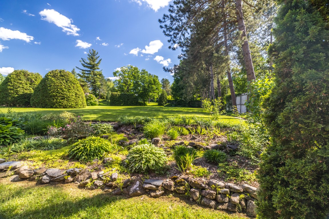 Grand jardin paysager avec massifs de fleurs, pierres et arbres matures à l'Espace du Carmel