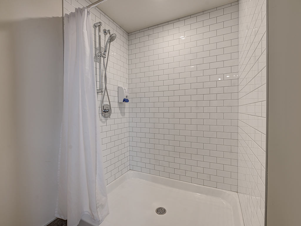 Douche avec carrelage blanc et pomme de douche amovible à l'Espace du Carmel