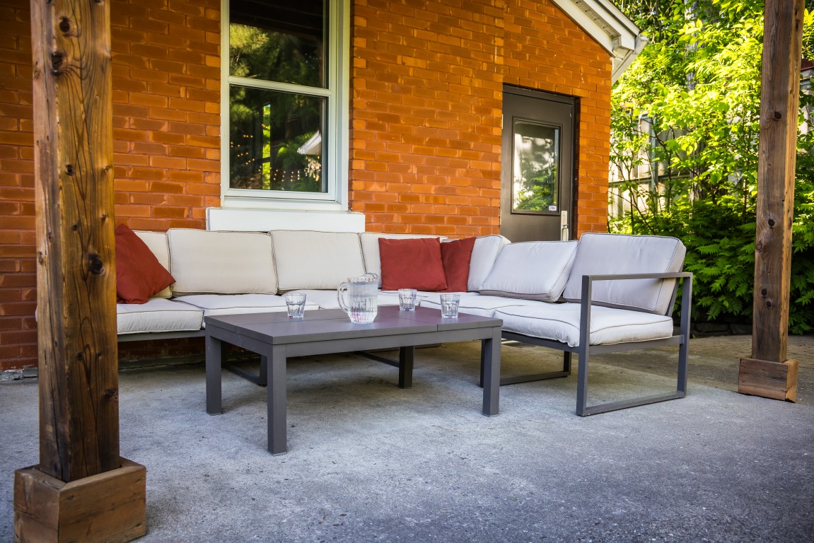 Terrasse couverte avec canapés extérieurs et table basse contre un mur de brique à l'Espace du Carmel